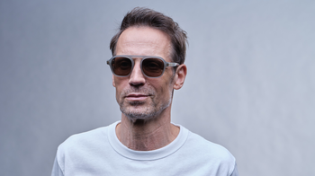 Das Bild zeigt einen Mann in weißem T-Shirt mit Designer-Sonnenbrille.